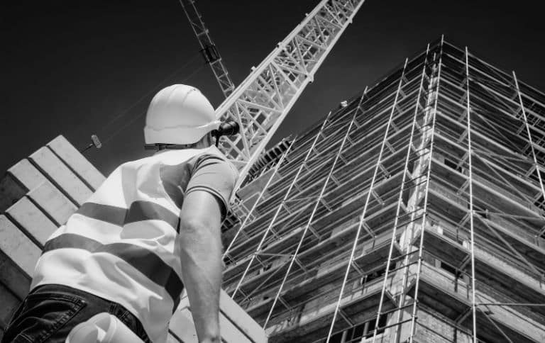 a construction worker looking up the building and crane above him